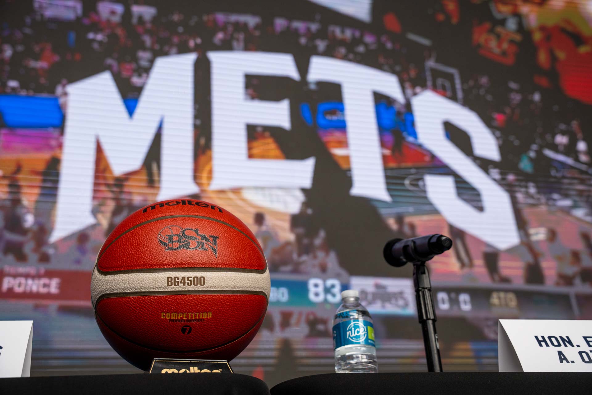 photo of a METS basketball on top of a press conference table with a METS game on a tv in the background